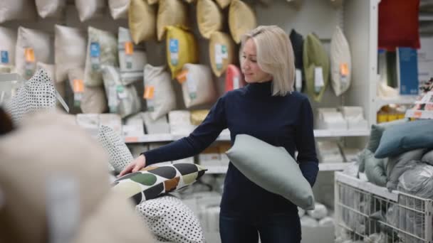 Mujer en una tienda de artículos para el hogar. La rubia elige almohadas para el interior de su apartamento — Vídeos de Stock