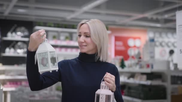 Жінка в магазині побутових товарів. Блондинка підбирає речі в інтер'єрі своєї квартири — стокове відео