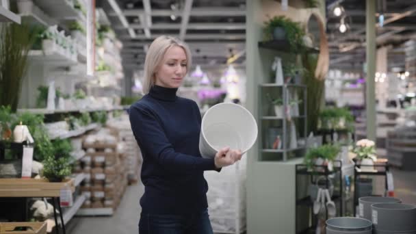 Giovane donna in un negozio di fiori. Bella bionda sceglie un vaso di fiori. — Video Stock