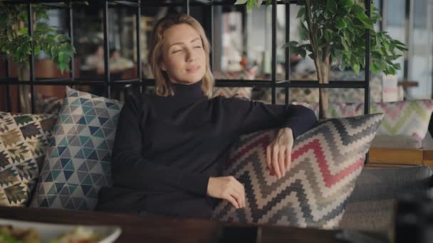 Porträt einer attraktiven Frau in einem Restaurant. Die Blondine sitzt, ruht sich aus und denkt über das Leben nach. — Stockvideo
