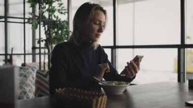 Çekici sarışın kadın bir kafede akıllı telefon kullanıyor. Bir kadın arkadaşlarıyla ve meslektaşlarıyla sohbet ediyor..