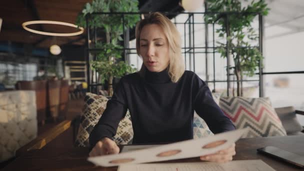 Aantrekkelijke vrouw in een café tijdens een zakenlunch. De blonde kijkt naar het menu. — Stockvideo