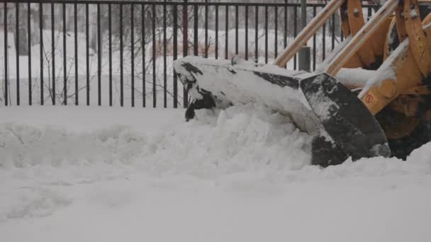 Emmer graafmachine reinigt de stad trottoir van sneeuw. Stadsdiensten ruimen de straten op tijdens sneeuwval. — Stockvideo