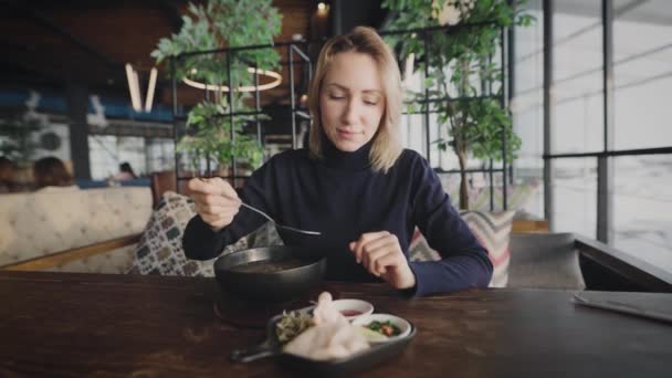 Attraktive Blondine in einem Restaurant. Eine Frau isst panasiatische Suppe. — Stockvideo