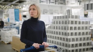 Geniş bir ev geliştirme mağazasında bir kadın. Alışveriş arabalı sarışın bir kadın büyük bir galeride yürüyor..