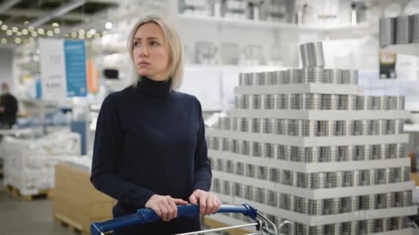 Une femme dans un grand magasin de rénovation. Une femme blonde avec un chariot marche à travers un grand showroom. — Video