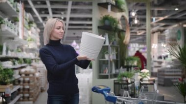 Çiçekçide genç bir kadın. Güzel sarışın bir saksı seçiyor..