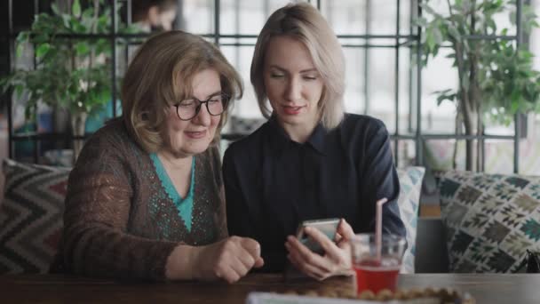 Μητέρα και κόρη συναντήθηκαν σε ένα εστιατόριο. Ηλικιωμένες και νέες γυναίκες χρησιμοποιούν εφαρμογές σε smartphone. — Αρχείο Βίντεο
