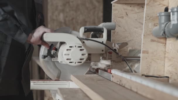 En el taller de carpintería. Un trabajador corta una tabla con una sierra de inglete. — Vídeos de Stock