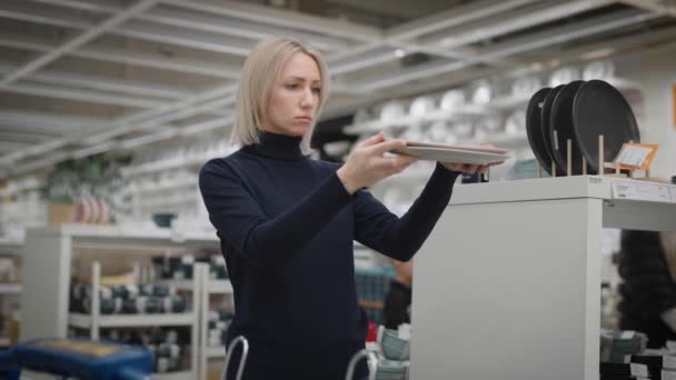 Jeune femme dans un magasin d'ustensiles. Les mains des femmes tiennent les plaques. — Video