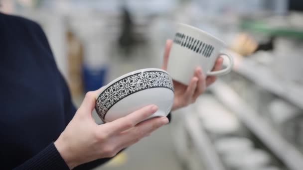 Jeune femme dans un magasin d'ustensiles. Les mains tiennent une tasse et une soucoupe. — Video