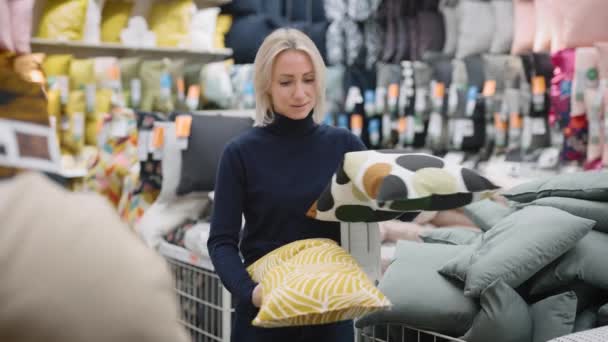 Een vrouw in een winkel. De blonde kiest kussens voor het interieur van haar appartement — Stockvideo