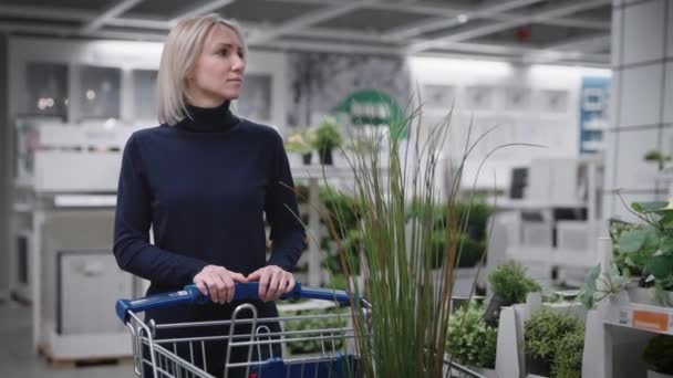 Досить молода жінка в магазині рослин. Блондинка вибирає озеленення для будинку . — стокове відео