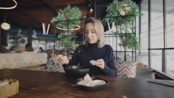 Atractiva rubia en un restaurante. Una mujer come sopa panasiática. — Vídeos de Stock