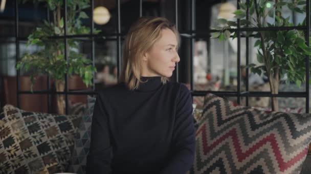 Porträt einer attraktiven Frau in einem Restaurant. Die Blondine sitzt, ruht sich aus und denkt über das Leben nach. — Stockvideo