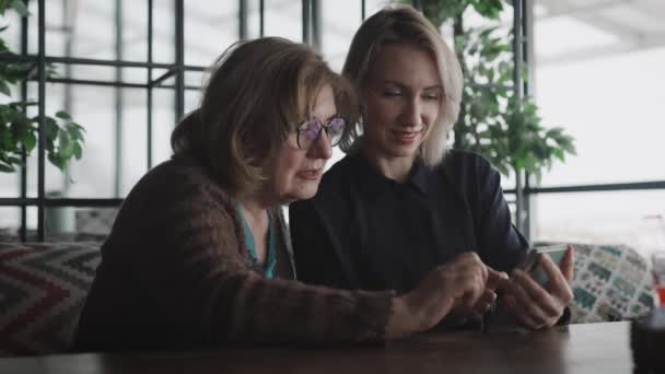 Mor och dotter träffades på en restaurang. Äldre och unga kvinnor använder appar i en smartphone. — Stockvideo