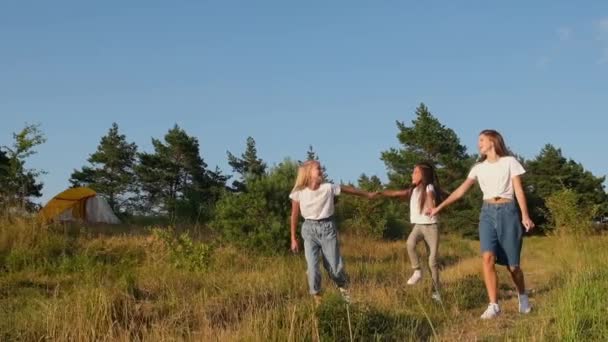 Trois filles heureuses s'amusent en vacances dans un camp avec des tentes dans les bois. — Video