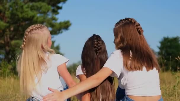 Tre flickor vänner sitter i en omfamning på en bakgrund av naturen. — Stockvideo