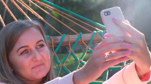Schöne junge Frau macht ein Selfie mit dem Handy, das in der Hängematte liegt. — Stockvideo