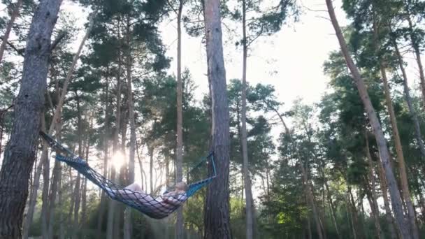 A lány egy függőágyban pihen egy fenyőerdőben.. — Stock videók