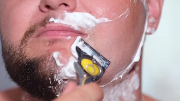 Man van de hand met een disposable scheermes scheert zijn gezicht close-up. — Stockvideo