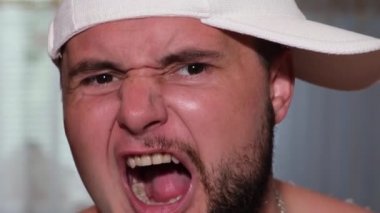 Genç bir adam rap okuyor, beyaz şapkalı ve tuhaf yüz ifadeleri gösteriyor.. 