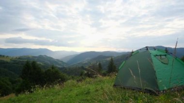 Turist çadırı, dağların arkasındaki yeşil çimlerin üzerinde duruyor..