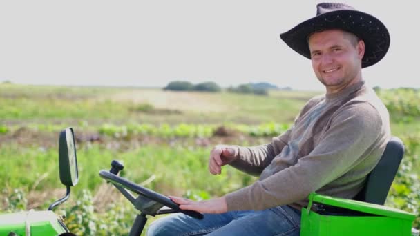 Portret van een lachende jonge bebaarde boer zittend op een kleine landbouwtrekker. — Stockvideo