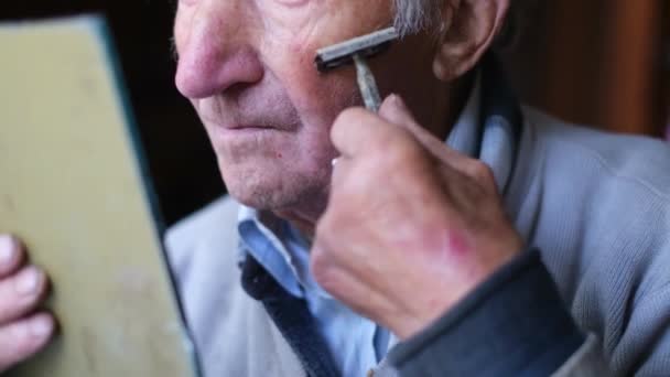 Een oudere man scheert zijn gezicht voor een spiegel. De gepensioneerde scheert zijn baard af.. — Stockvideo
