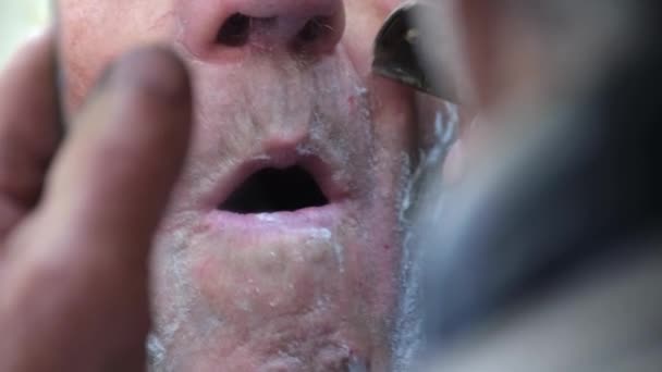 Een oudere man scheert zijn gezicht voor een spiegel. De gepensioneerde scheert zijn baard af.. — Stockvideo