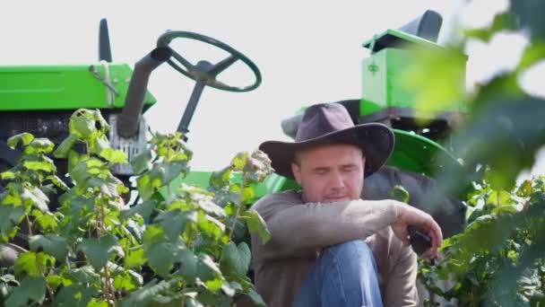 Un fermier fatigué se reposant près d'un tracteur. Dépression dans un homme de la campagne. — Video
