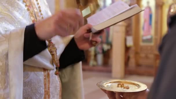 Un sacerdote en la iglesia durante la ceremonia de boda consagra anillos de bodas de oro para la novia — Vídeo de stock