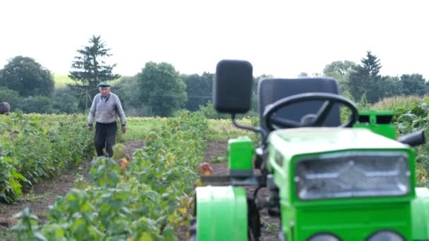 Der Rentner arbeitet im Garten in der Nähe seines Hauses. Ein alter Bauer mit seinem Traktor. — Stockvideo
