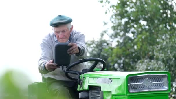 Hombre retirado en su mini-tractor. Un trabajador del pueblo trabaja en su campo — Vídeo de stock