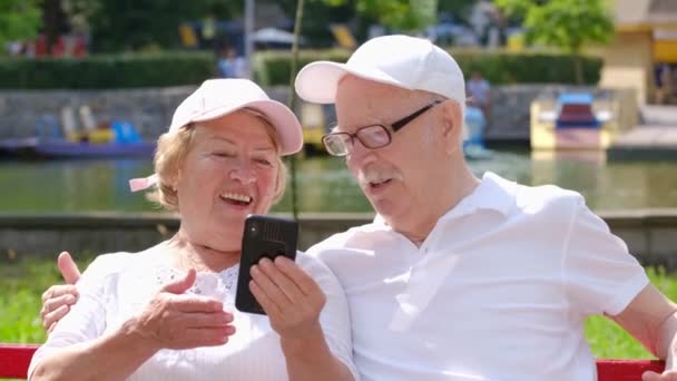 Glückliches Senioren-Paar mit Smartphone macht Selfie und umarmt sich im Park. — Stockvideo