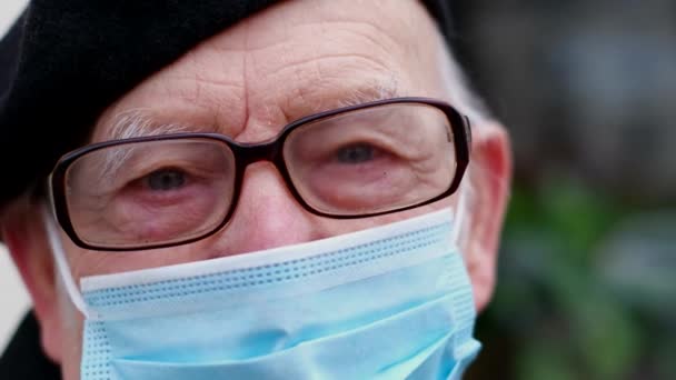 Een oude grootvader met een beschermend masker loopt door de straten van de stad — Stockvideo