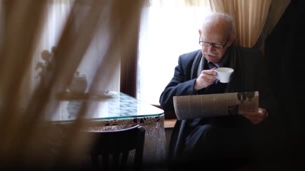 新聞を読んでいるカフェのテーブルに座ってコーヒーを持っているシニア男. — ストック動画