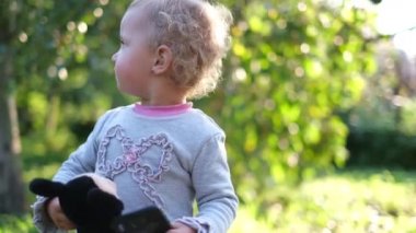 Küçük bir çocuk elinde akıllı bir telefon ve yumuşak bir oyuncak tutarak dans ediyor.