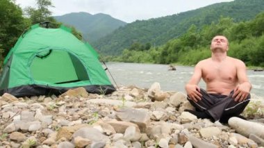 Şişman bir adam yeşil çadırın yanında yoga yapıyor..