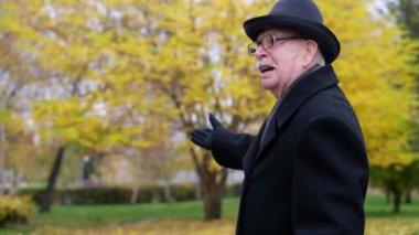 Yaşlı büyükbaba yan tarafı işaret ediyor. Emekli adam parkta yürüyor.