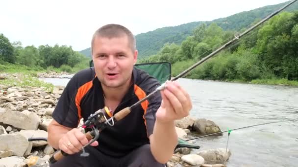 Un pescador masculino bloguea y le dice a la cámara sobre los señuelos de pesca. — Vídeos de Stock