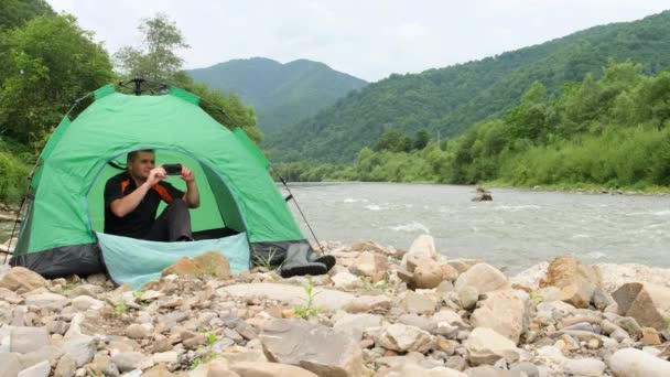 テントの中の観光客は、スマートフォンで山の川の美しい景色を捉えます。. — ストック動画