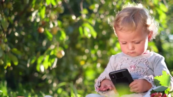 Malá holčička si hraje v jablečném sadu, sedí na zelené trávě. — Stock video