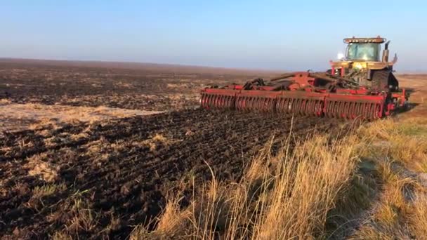 Un tractor araña y arrasa la tierra en un campo grande en un día soleado de primavera. — Vídeos de Stock