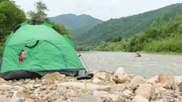 El turista se despierta en una tienda cerca de un río de montaña. — Vídeos de Stock