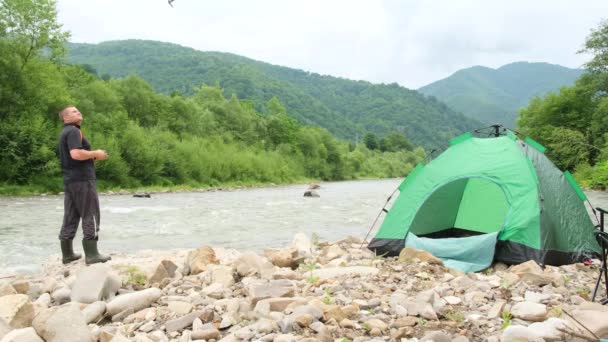 Um homem controla um drone de férias perto de um rio de montanha. — Vídeo de Stock