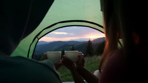 Jovem casal sentado em uma tenda de acampamento turístico com uma xícara de chá quente. — Vídeo de Stock