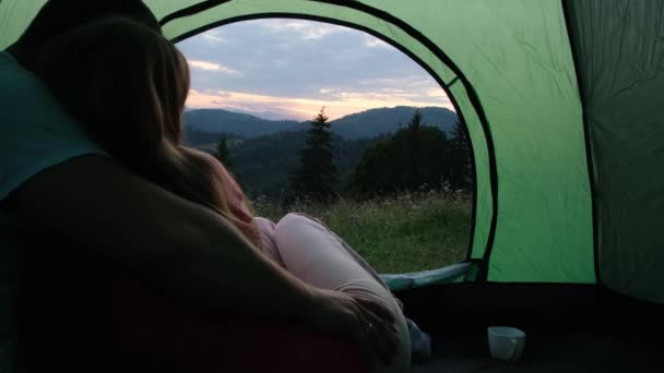 Een liefhebbend stel in een omhelzing bewondert de zonsondergang. Nacht kamperen in de bergen. — Stockvideo