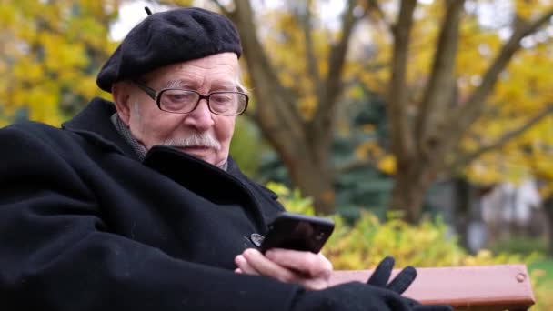 Un abuelo con bigote gris y una boina negra está hablando en un smartphone — Vídeos de Stock