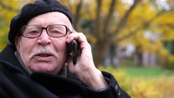 Ein Großvater mit grauem Schnurrbart und schwarzer Baskenmütze spricht auf einem Smartphone — Stockvideo